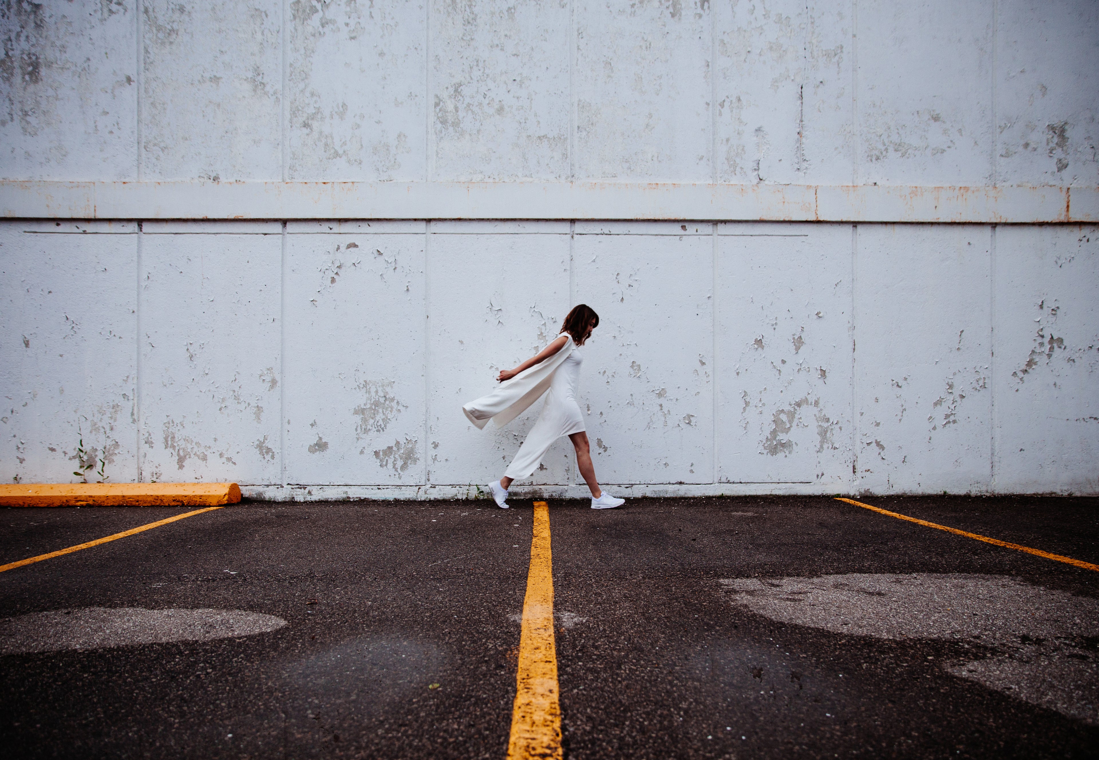 Woman in white dress walking outdoors against a concrete wall — HYFN